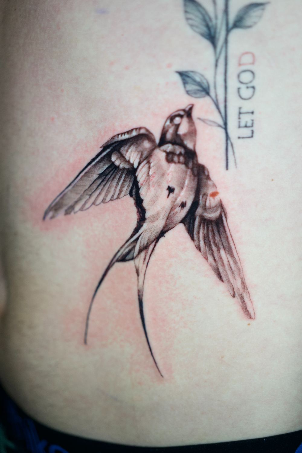fine line swallow rib tattoo with red accent by Antwan Rodriguez, West Palm Beach FL